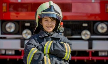 Boy dressed in a fire fighters uniform in front of a fire truck at a fire station